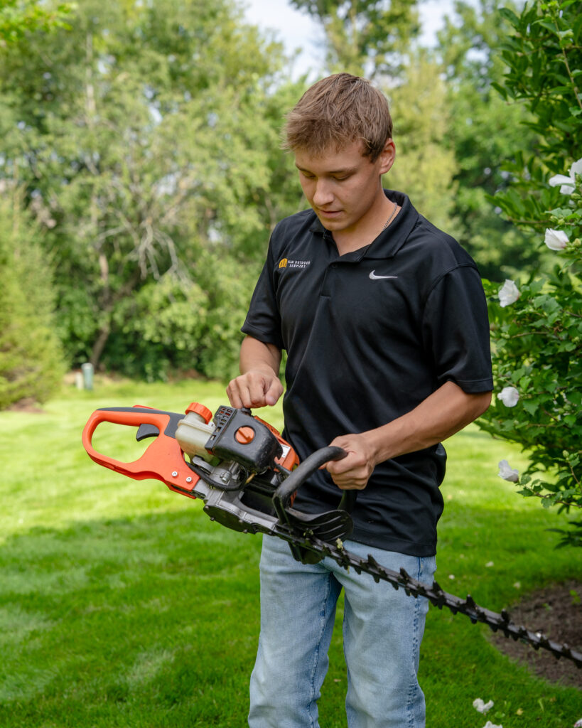 HLM crew member trimming a hedge with a power trimmer
